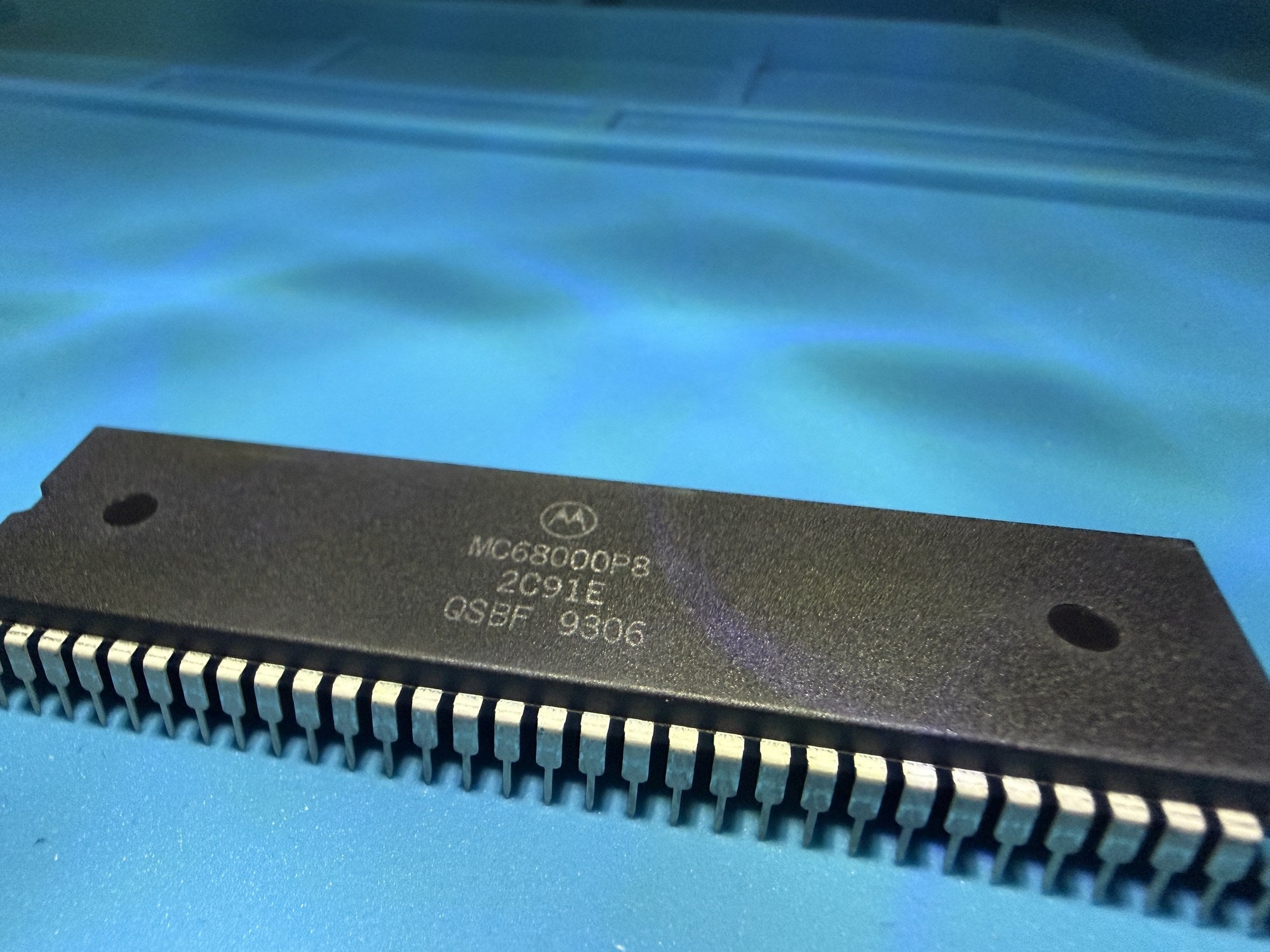 Close-up of a Motorola MC68000P8 microprocessor, whole chip, on a blue background.