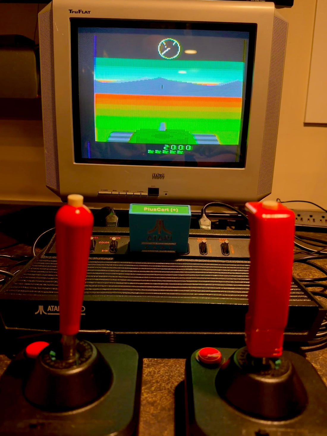 Atari 2600 running Battlezone TC on a CRT with two joysticks and a PlusCart+ cartridge.