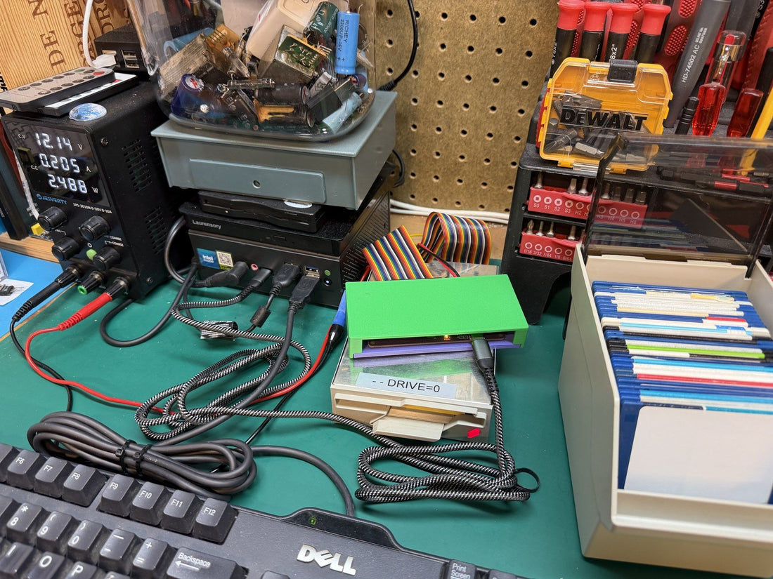 Greaseweazle V4.1 floppy-writing rig on a workbench: bench power supply, mini PC, 3.5-inch drive, and disk caddy.